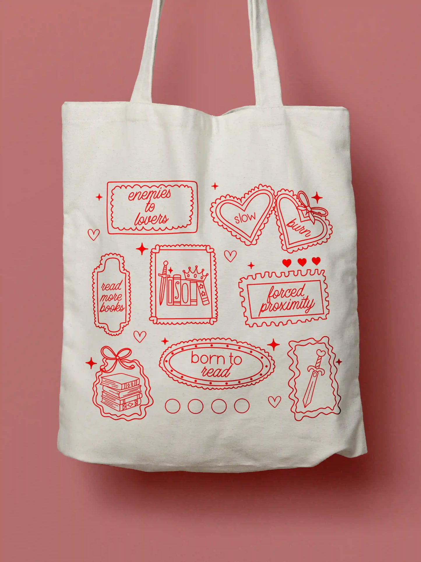 A canvas tote bag featuring red line-art illustrations styled as vintage stamps, with bookish phrases and tropes including "enemies to lovers," "slow burn," "read more books," "forced proximity," and "born to read," alongside drawings of books, a crown, a sword, and decorative hearts and sparkles. Photographed against a red background.
