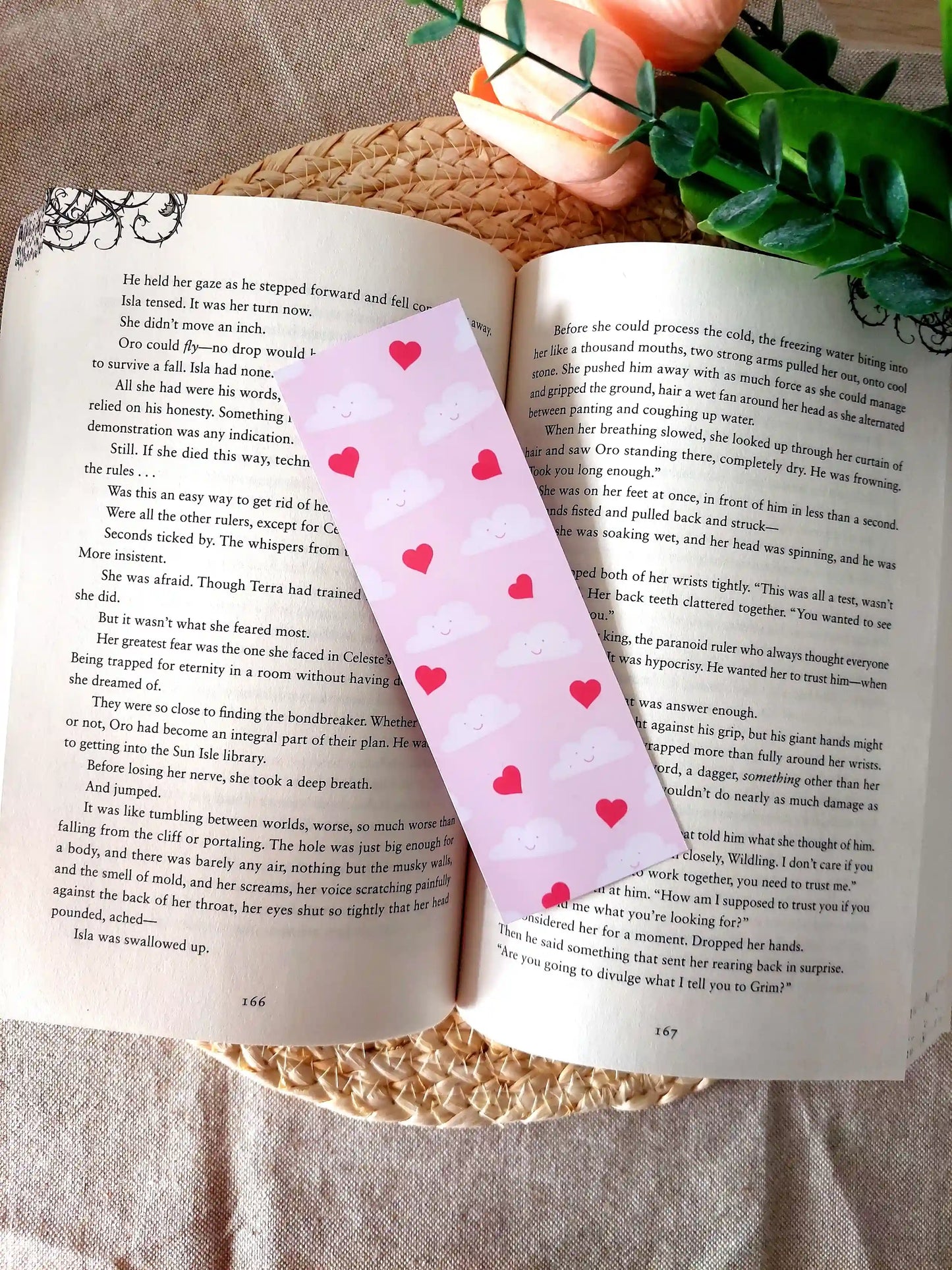 Bookmark featuring a pattern with smiling clouds and red hearts on a pink background, resting on an open book.