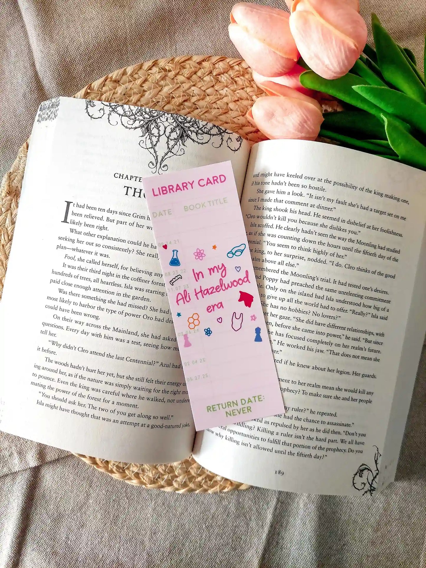 Bookmark designed like a library card, with the text “In my Ali Hazelwood era”, and small themed illustrations, resting on an open book.