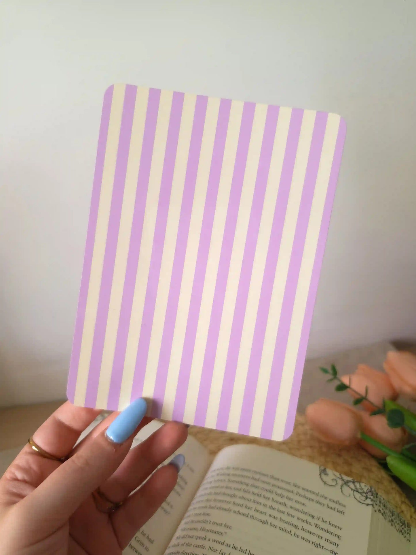 A hand holding an e-reader insert with soft lavender and cream vertical stripes.