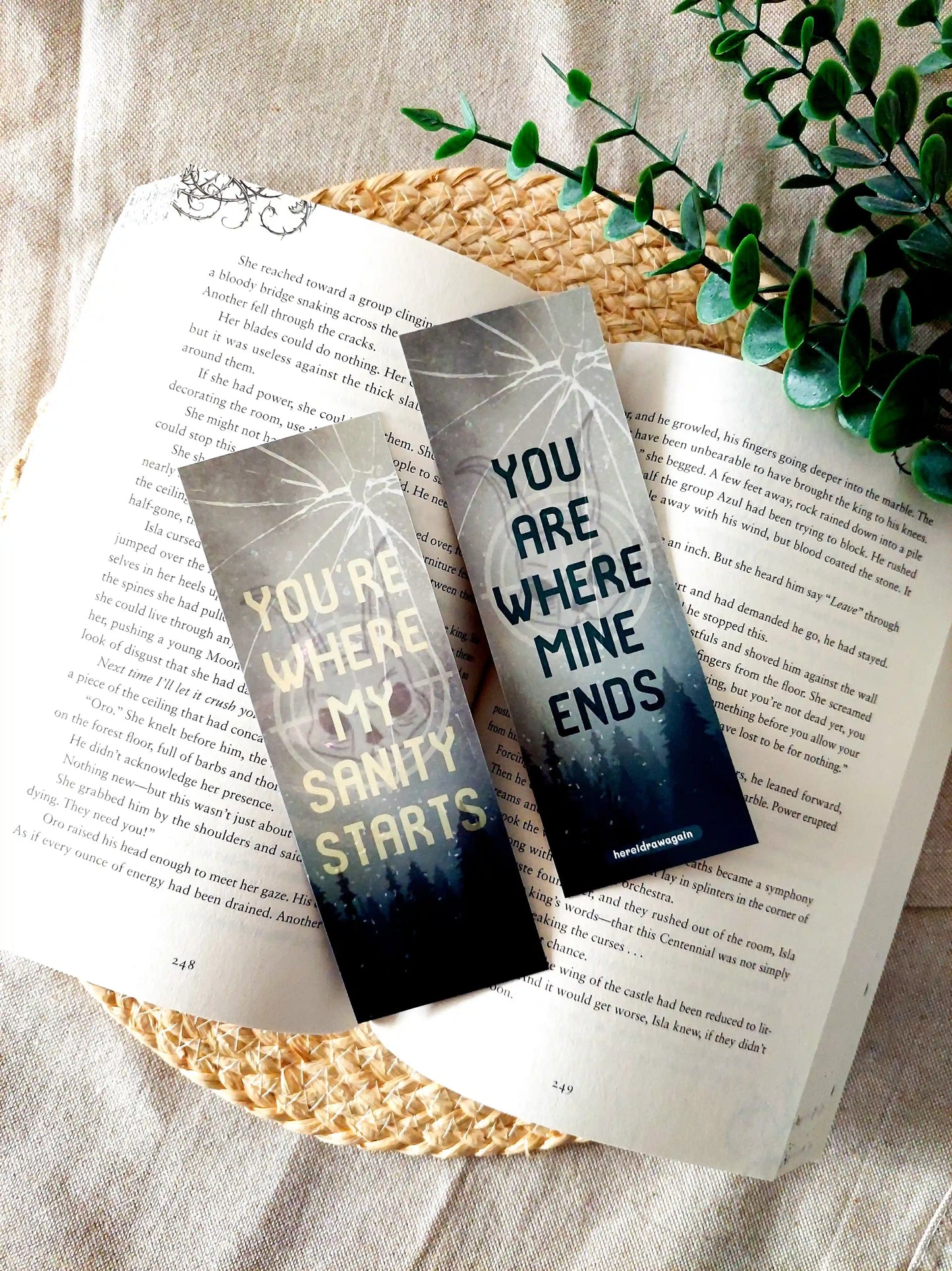 Leave Me Behind inspired bookmark displayed on an open book, featuring a forest and cracked glass design with the quote "You're where my sanity starts" and "You are where mine ends" split across front and back.