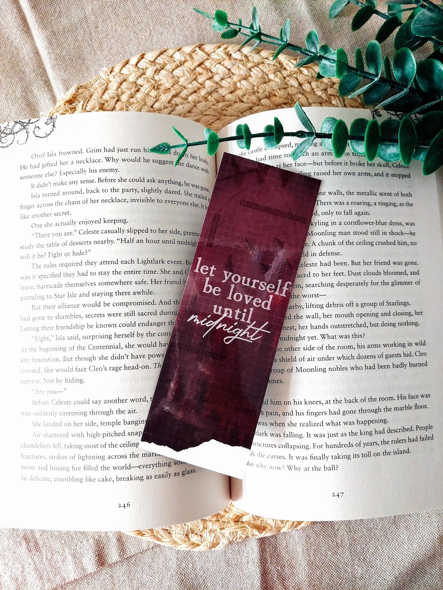 Nightshade bookmark placed on an open book, featuring a dark burgundy background with flying birds, a crossword pattern with book-related words and the text "Let yourself be loved until night" in white.