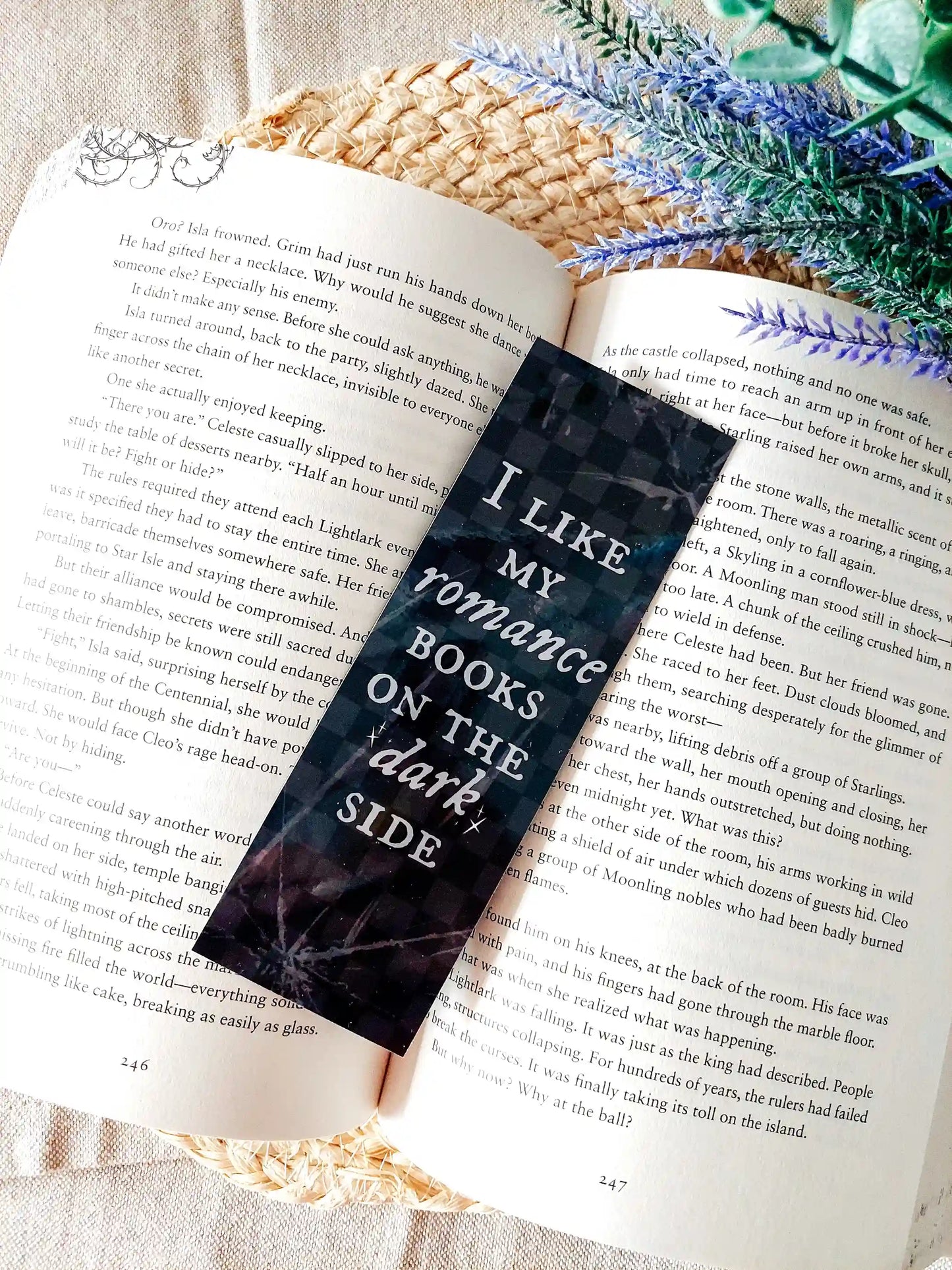 Book with a bookmark reading "I Like My Romance Books On The Dark Side" placed on an open book, featuring a dark checkered marble pattern with white text and brokeen glass details.