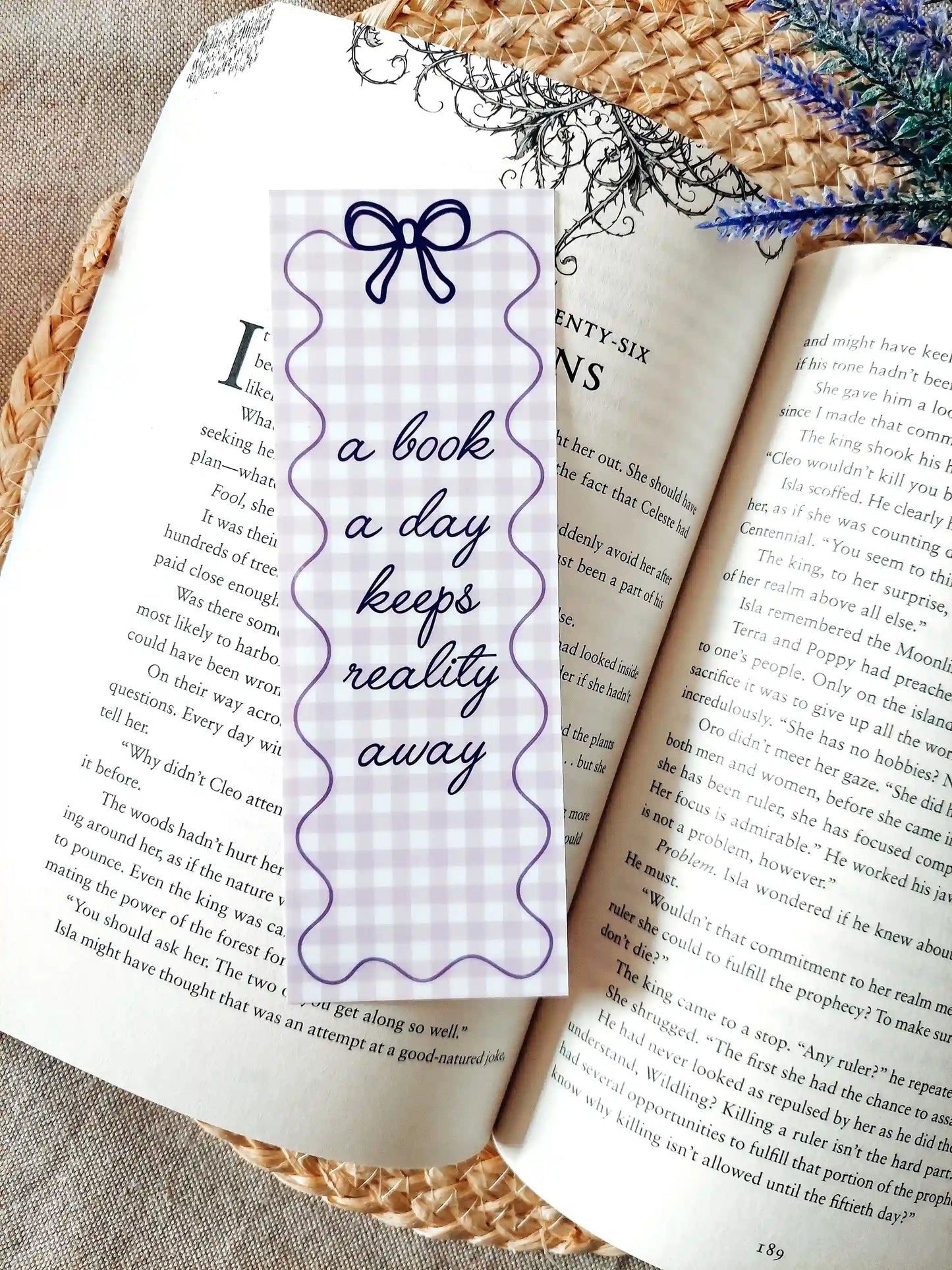 Illustrated bookmark with the text "A book a day keeps reality away", featuring a purple gingham pattern and decorative border, placed on an open book.