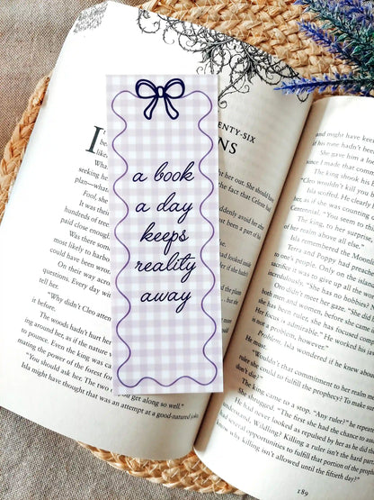 Illustrated bookmark with the text "A book a day keeps reality away", featuring a purple gingham pattern and decorative border, placed on an open book.