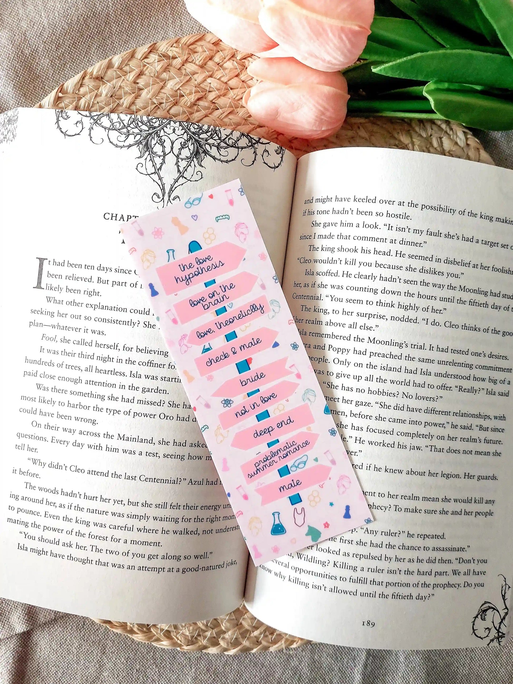 Bookmark showing Ali Hazelwood book titles arranged like a direction signpost with small themed illustrations, resting on an open book.