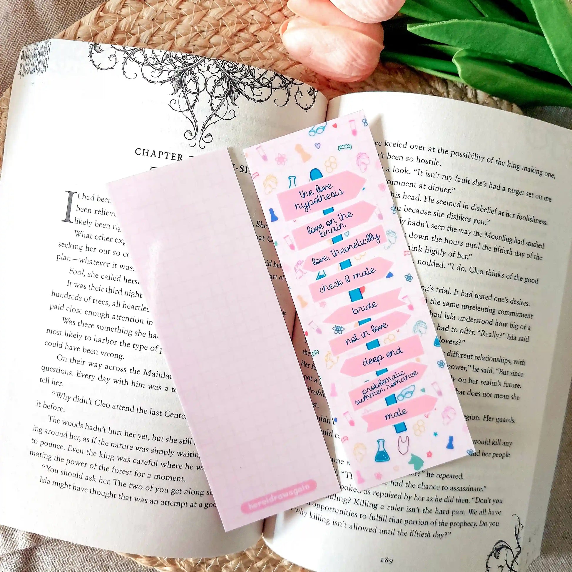 Bookmark showing Ali Hazelwood book titles arranged like a direction signpost with small themed illustrations, resting on an open book.