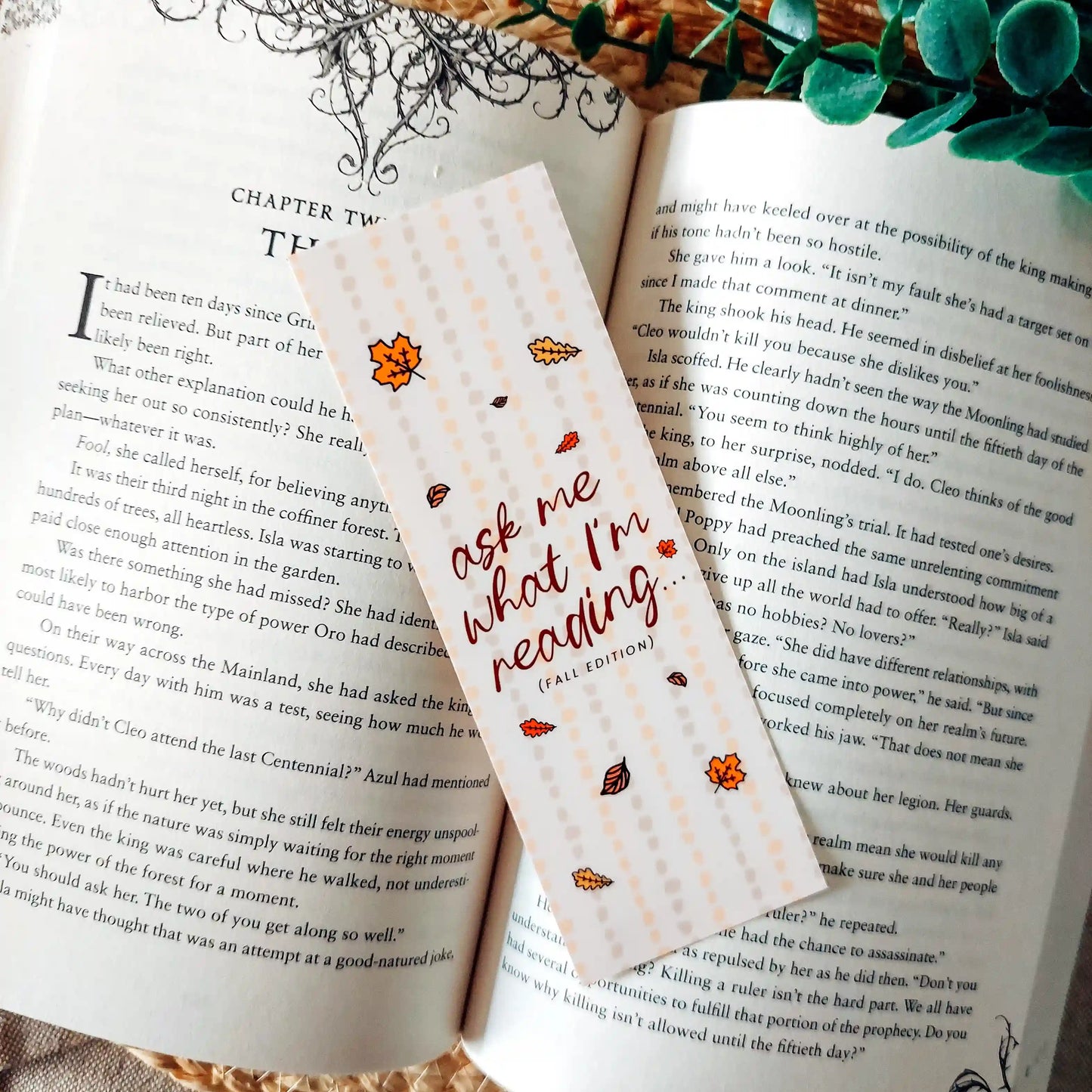 Illustrated bookmark in warm autumn colours with the text "Ask Me What I’m Reading" decorated with autumn leaves and placed on an open book.