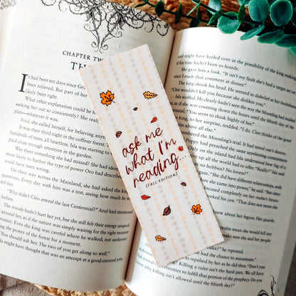 Illustrated bookmark in warm autumn colours with the text "Ask Me What I’m Reading" decorated with autumn leaves and placed on an open book.
