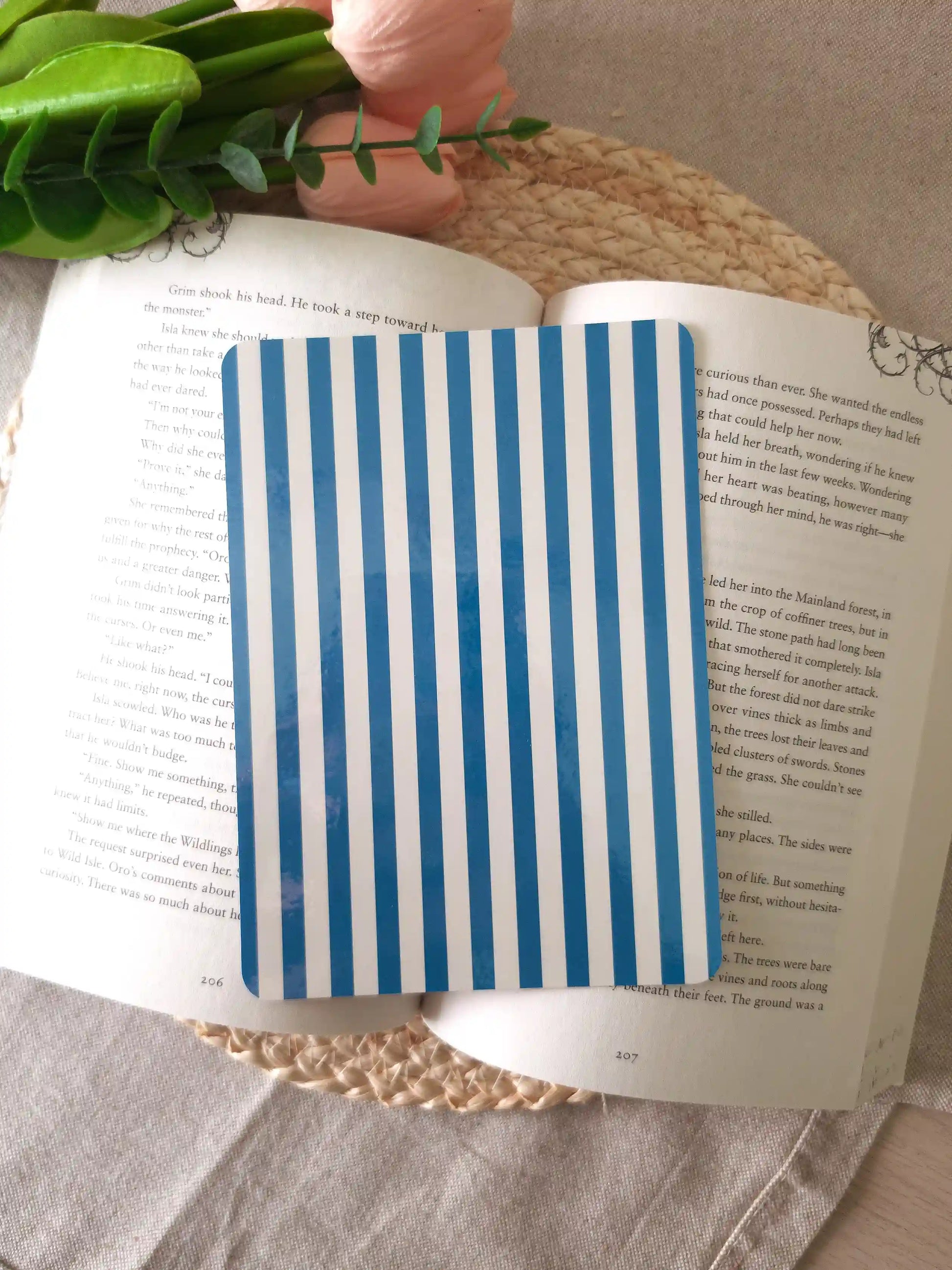 An e-reader insert with bold blue and white vertical stripes, placed on an open book resting on a woven rattan mat.