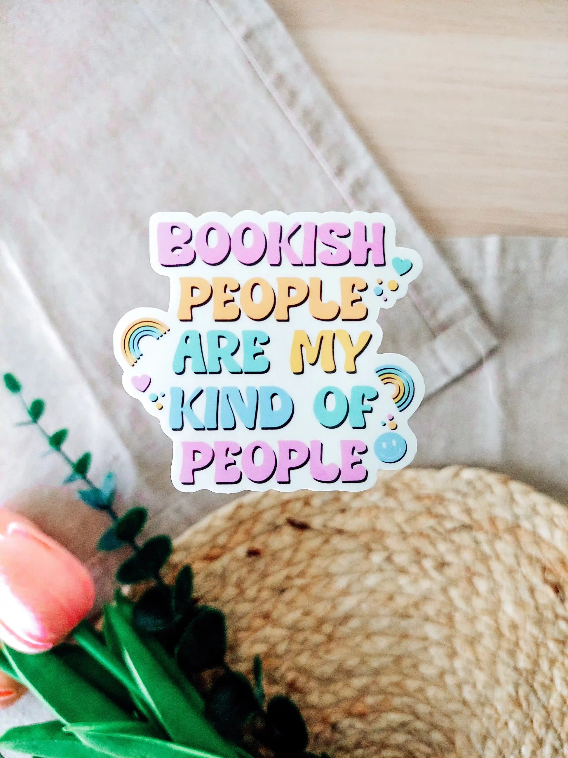 Colorful pastel vinyl sticker "Bookish people are my kind of people" shown on a textured woven surface.