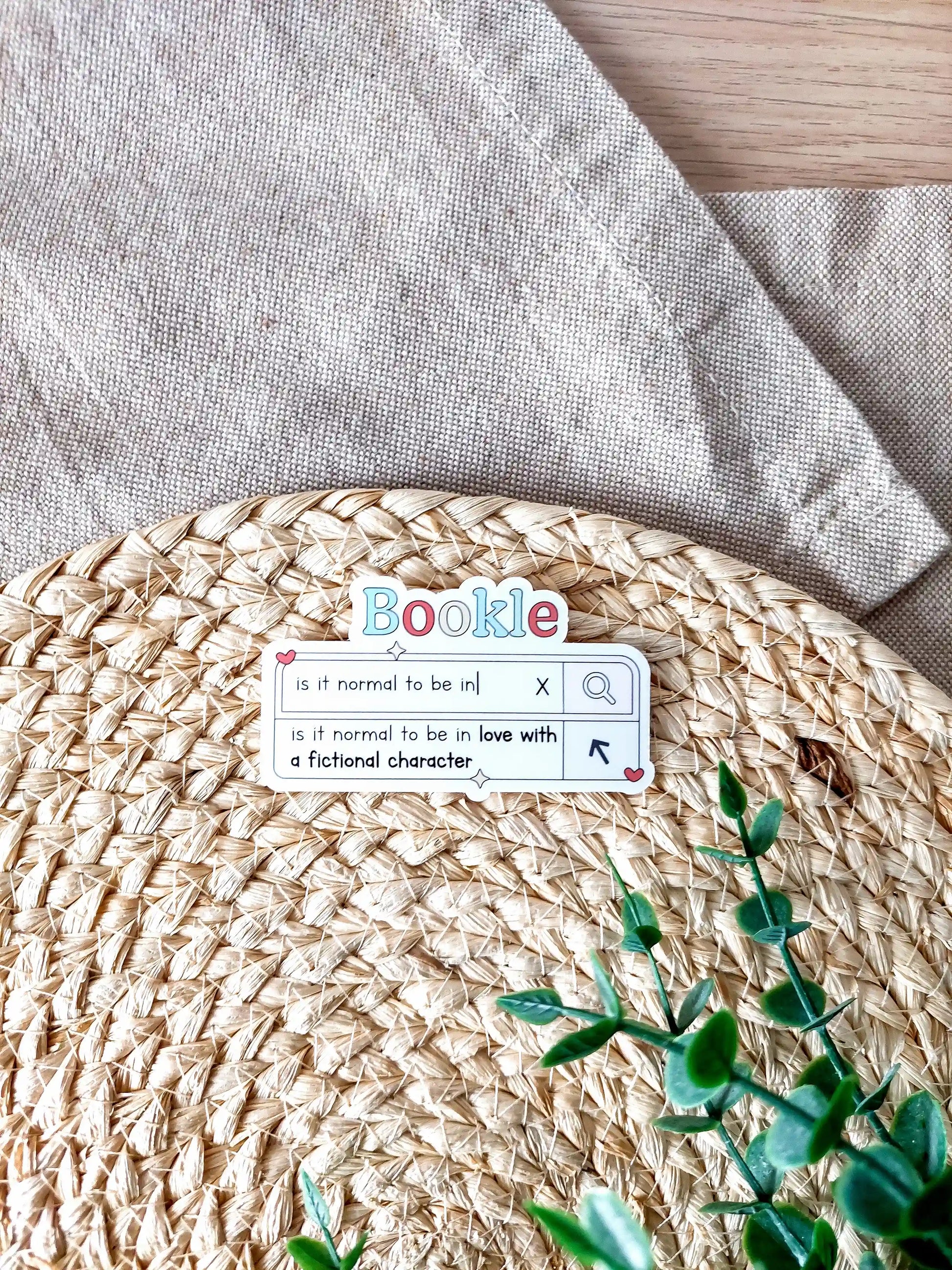 Vinyl sticker designed like a search bar with the text "is it normal to be in love with a fictional character", photographed on a woven background.