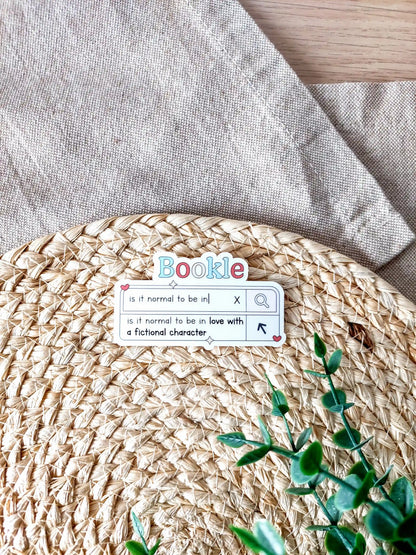 Vinyl sticker designed like a search bar with the text "is it normal to be in love with a fictional character", photographed on a woven background.