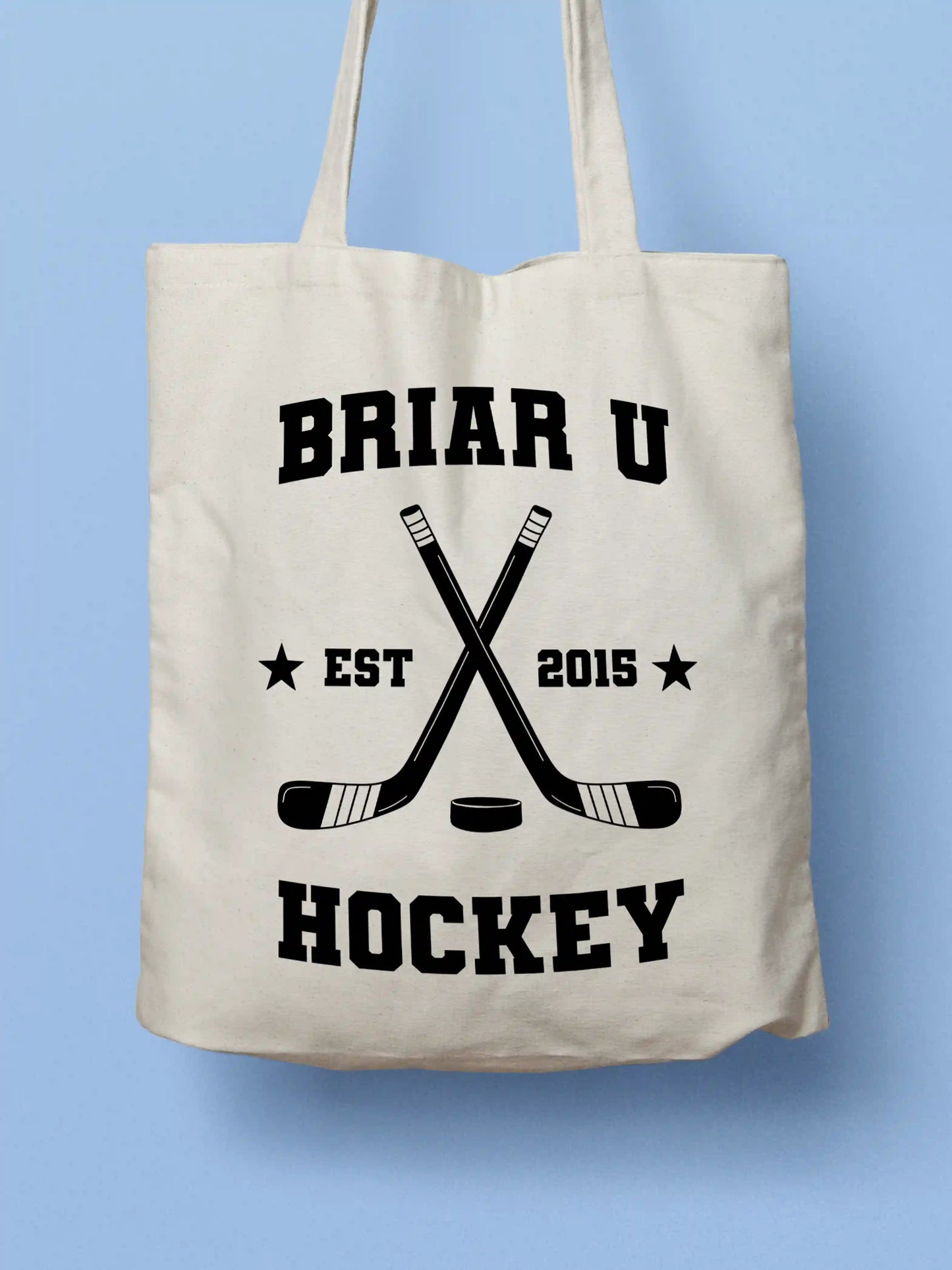 A white canvas tote bag featuring a "Briar U Hockey Est. 2015" design with crossed hockey sticks and a puck in black collegiate-style lettering, photographed against a light blue background.