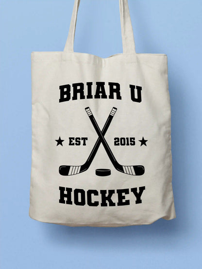 A white canvas tote bag featuring a "Briar U Hockey Est. 2015" design with crossed hockey sticks and a puck in black collegiate-style lettering, photographed against a light blue background.