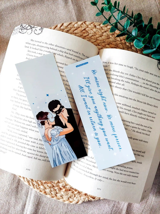 Bookmark inspired by Bridgerton featuring an illustration of Sophie and Benedict on the front and the quote "Be mine right now. Be mine forever. I'll give you anything you want. All I want in return is you" on the back, displayed on an open book over a woven mat with decorative plants. 