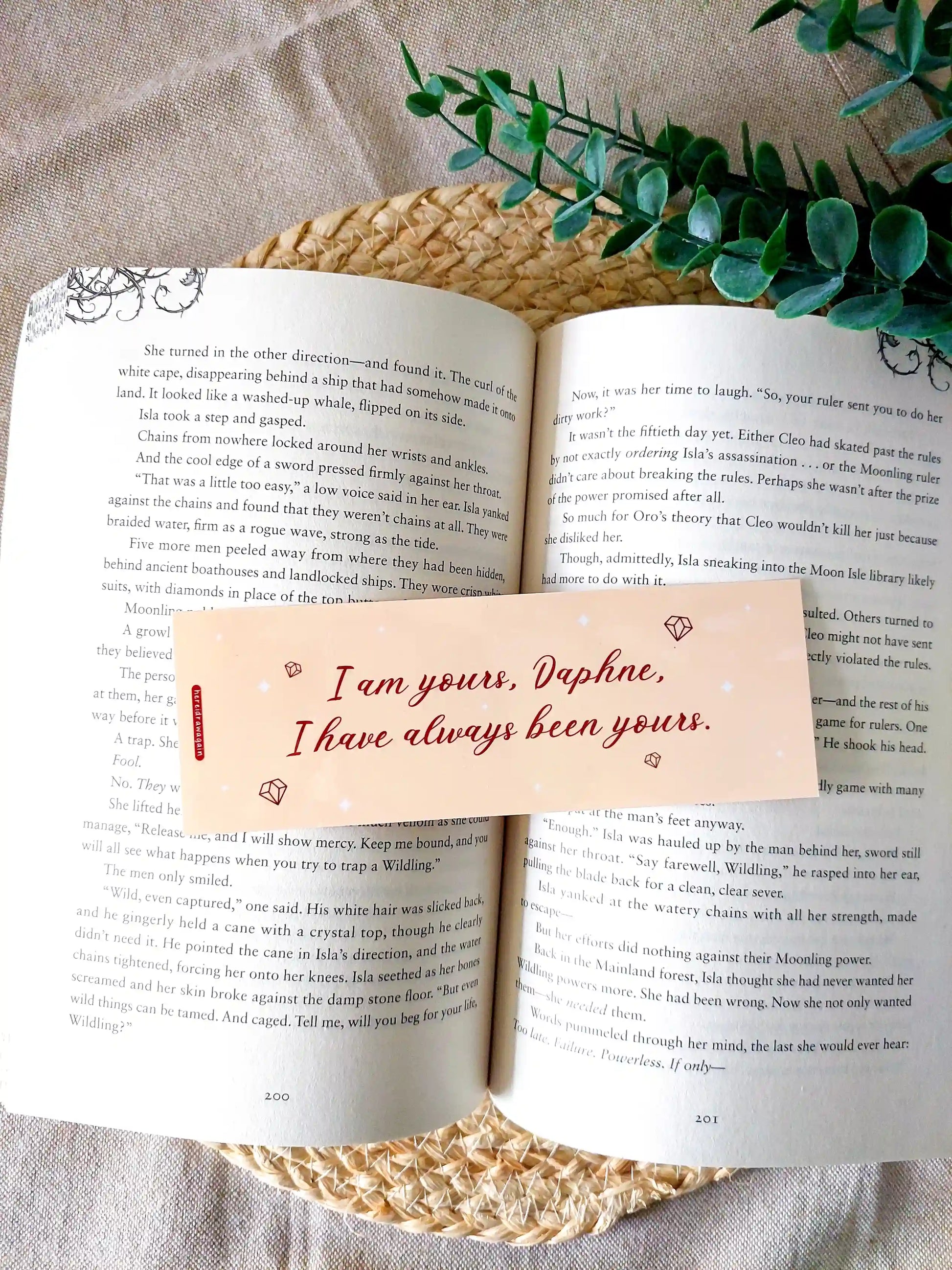 Bookmark inspired by Bridgerton featuring the quote "I am yours, Daphne. I have always been yours", displayed on an open book over a woven mat with decorative plants. 