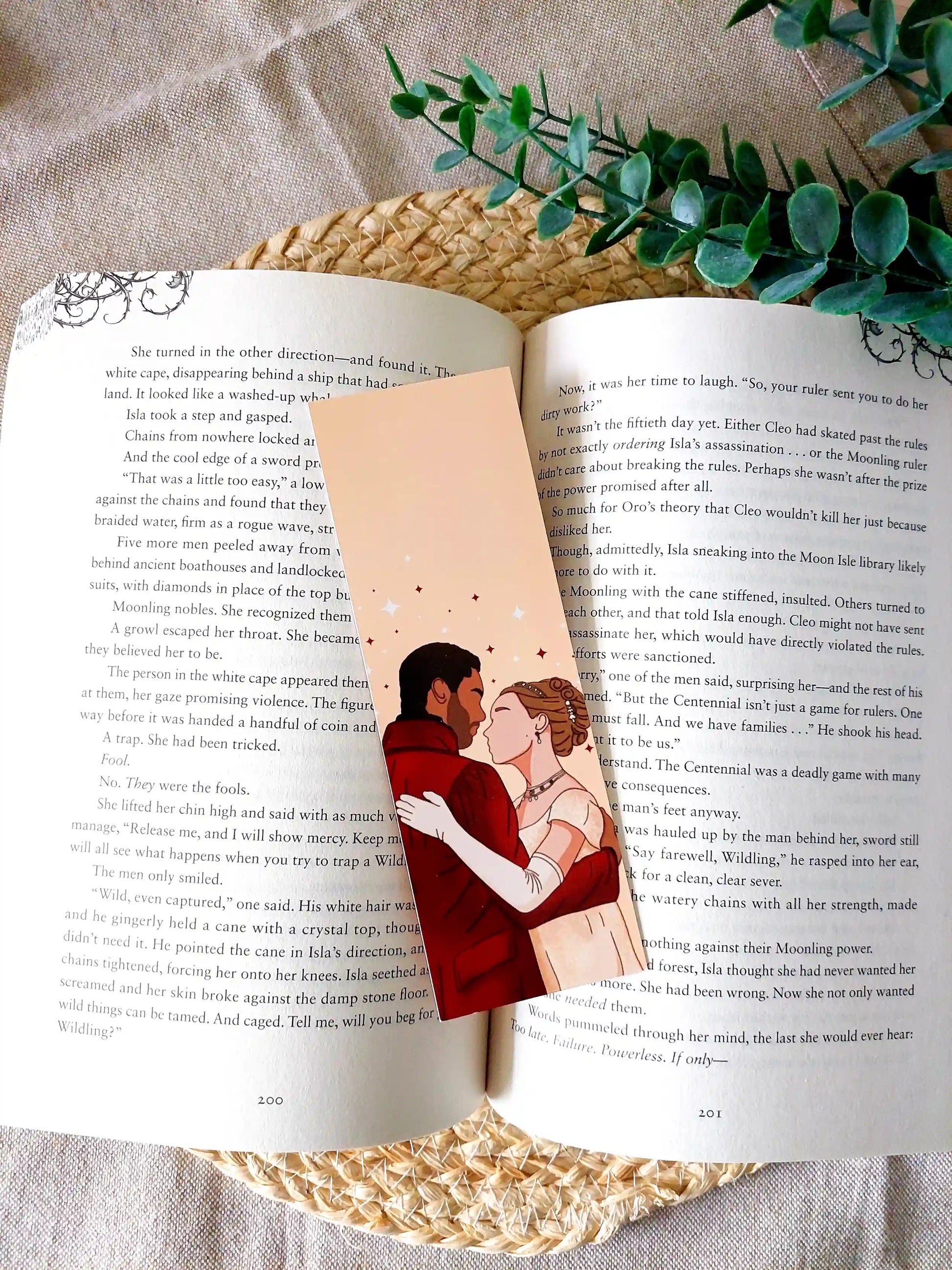 Bookmark inspired by Bridgerton featuring an illustration of Daphne and Simon, displayed on an open book over a woven mat with decorative plants. 