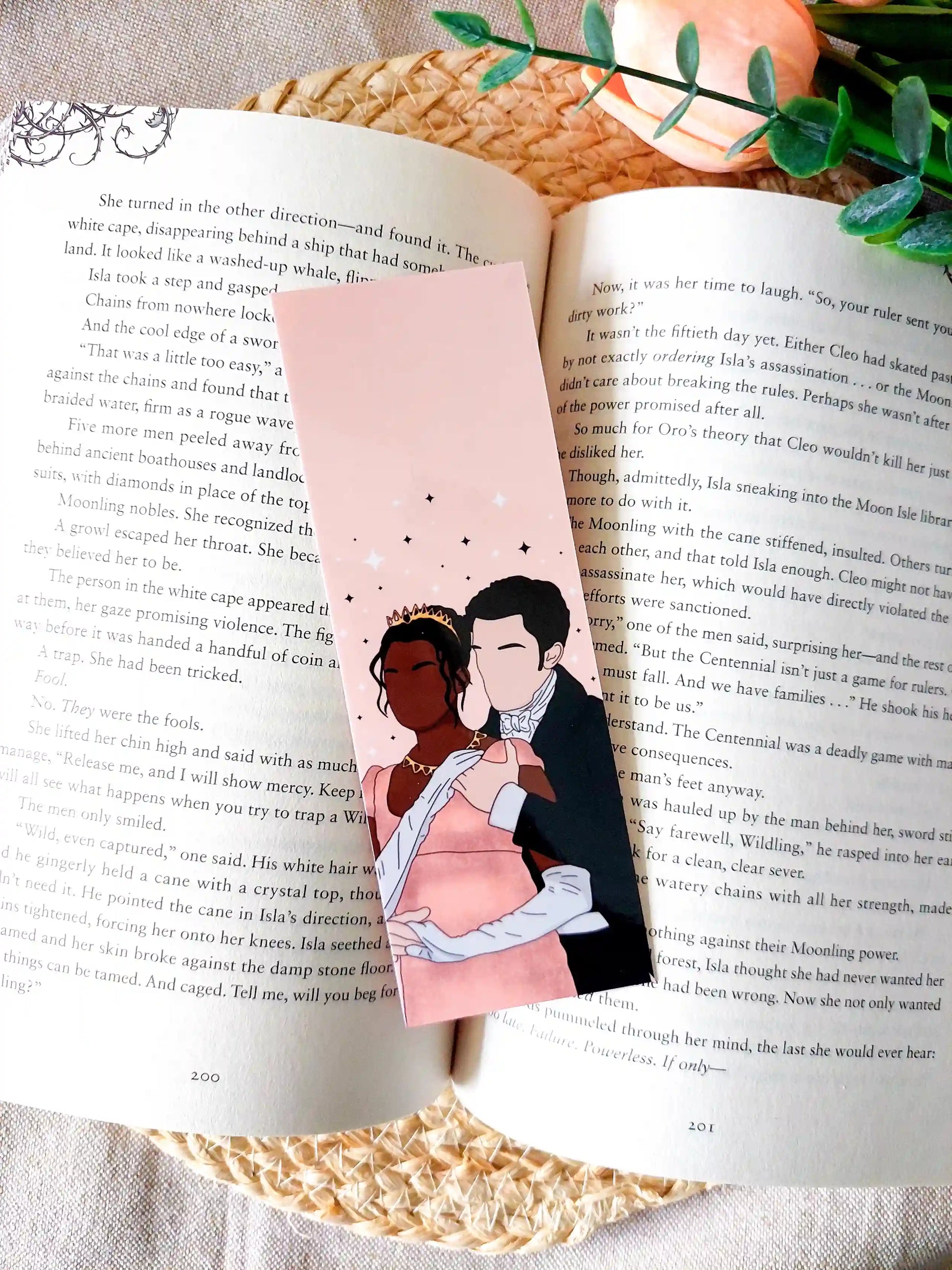 Bookmark inspired by Bridgerton featuring an illustration of Kate and Anthony, displayed on an open book over a woven mat with decorative plants. 
