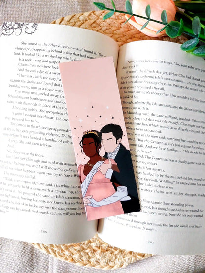 Bookmark inspired by Bridgerton featuring an illustration of Kate and Anthony, displayed on an open book over a woven mat with decorative plants. 