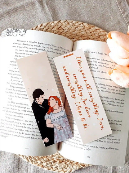 Bookmark inspired by Bridgerton featuring an illustration of Penelope and Colin on the front and the quote "I love you with everything I am, everything I've been and everything I hope to be" on the back, displayed on an open book over a woven mat with decorative plants. 