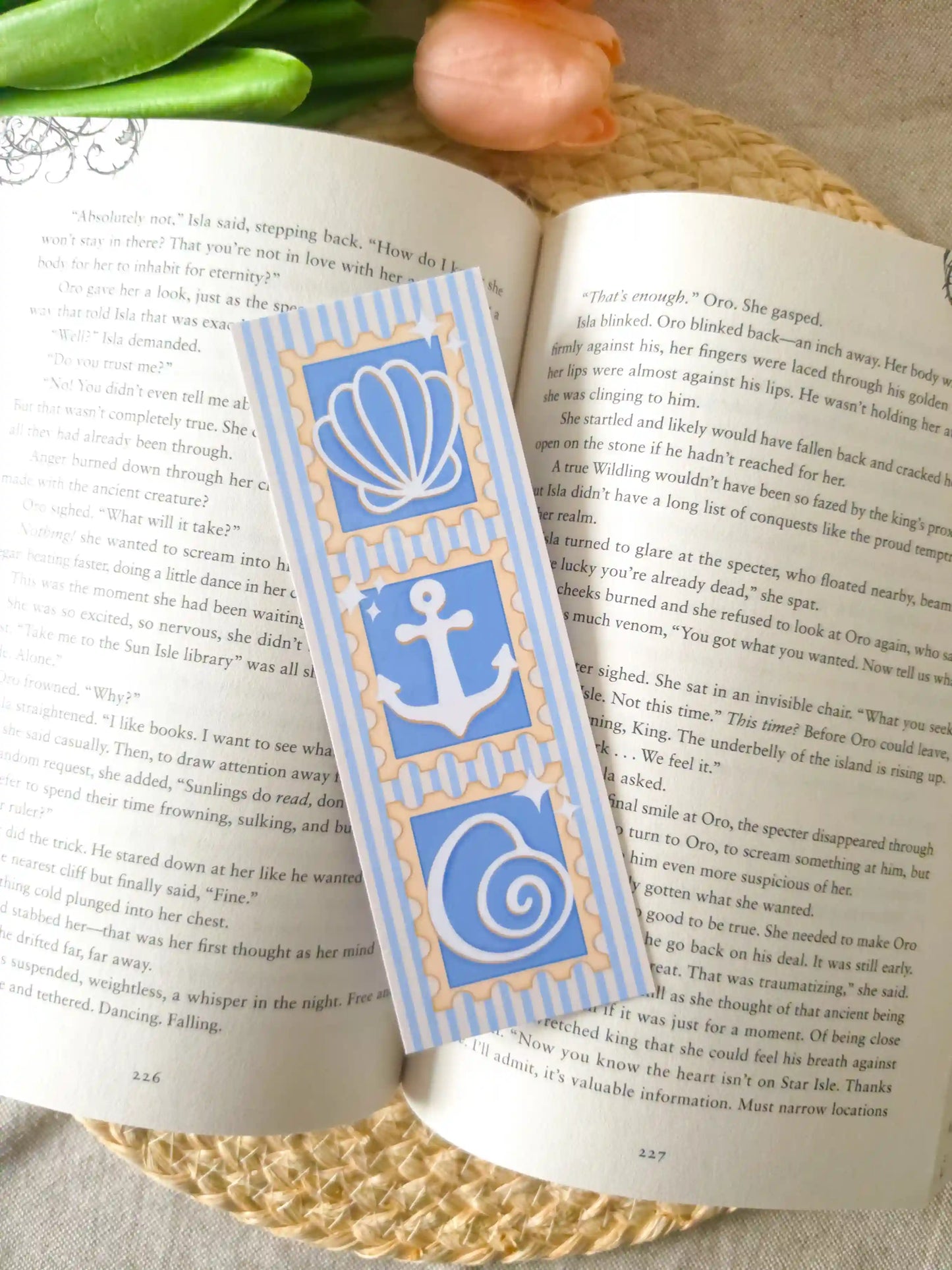 An open book featuring a bookmark with blue beachy stamp-like illustrations (a seashell, anchor and a shell) on a striped blue and white background.