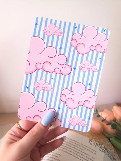 A hand holding an E-Reader insert with a light blue and white striped background covered in large fluffy pink clouds and small blue star details.