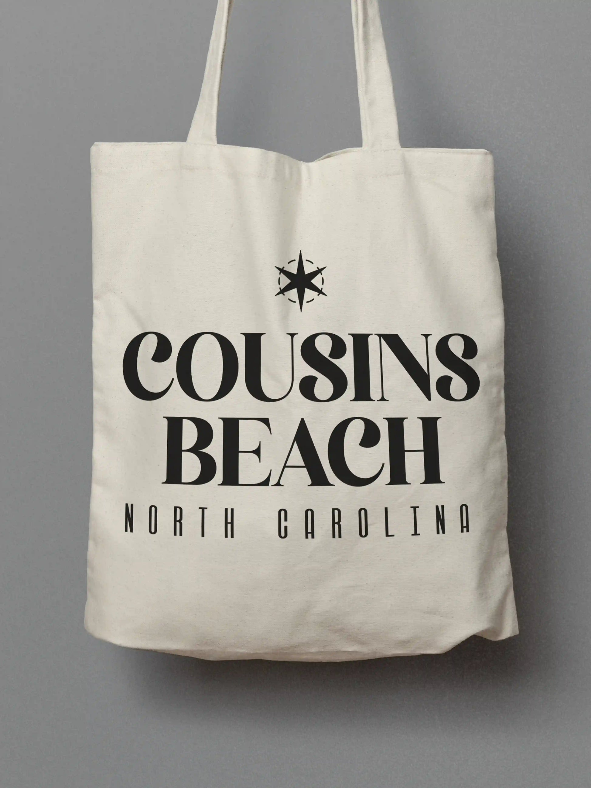 Cotton canvas tote bag with black "Cousins Beach, North Carolina" text, photographed on a solid gray background.