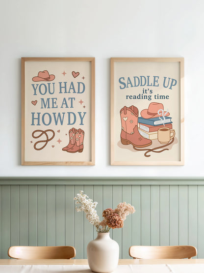 Set of two art prints inspired by cowboy romance books, featuring western-themed illustrations and the text "You Had Me at Howdy" on one and "Saddle Up, it’s reading time" on the other, displayed side by side in frames.