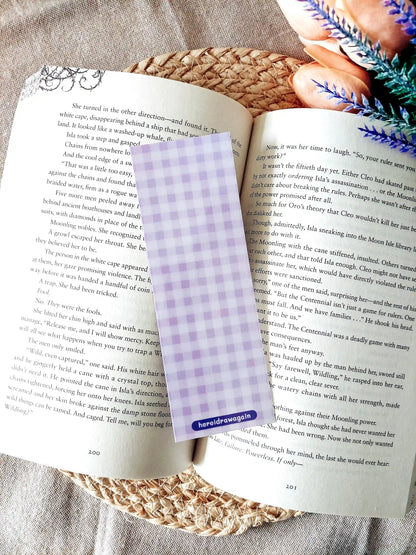Bookmark featuring a purple gingham pattern, displayed on an open book over a woven mat. 