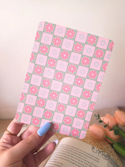 A hand holding an e-reader insert with a pink and sage green checkerboard pattern, each square featuring a pink or blue daisy illustration.