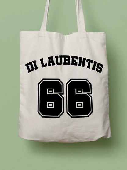 A white canvas tote bag featuring "Di Laurentis 66" in bold black collegiate-style lettering, photographed against a lavender background.