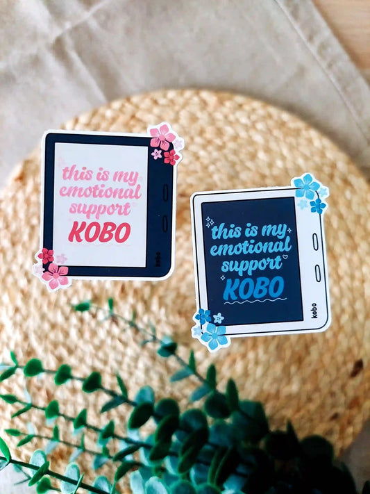 Two stickers of a Kindle with the phrase This is my emotional support Kobo" in black and whitecolor variants, photographed on a woven mat.