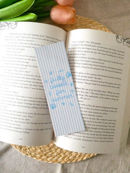 A striped bookmark with blue text reading "Fully booked for summer" and small blue illustrations, placed across an open book.
