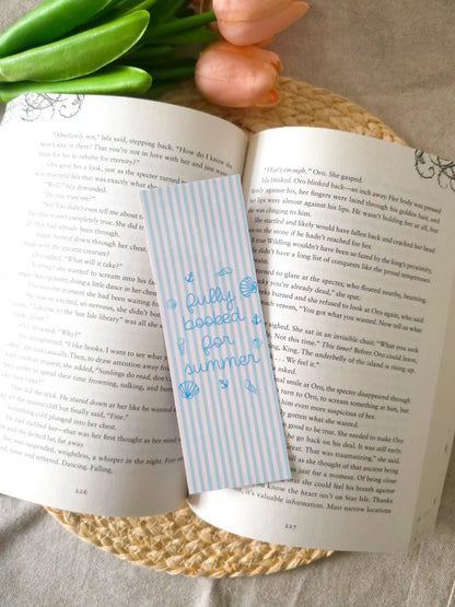 A striped bookmark with blue text reading "Fully booked for summer" and small blue illustrations, placed across an open book.