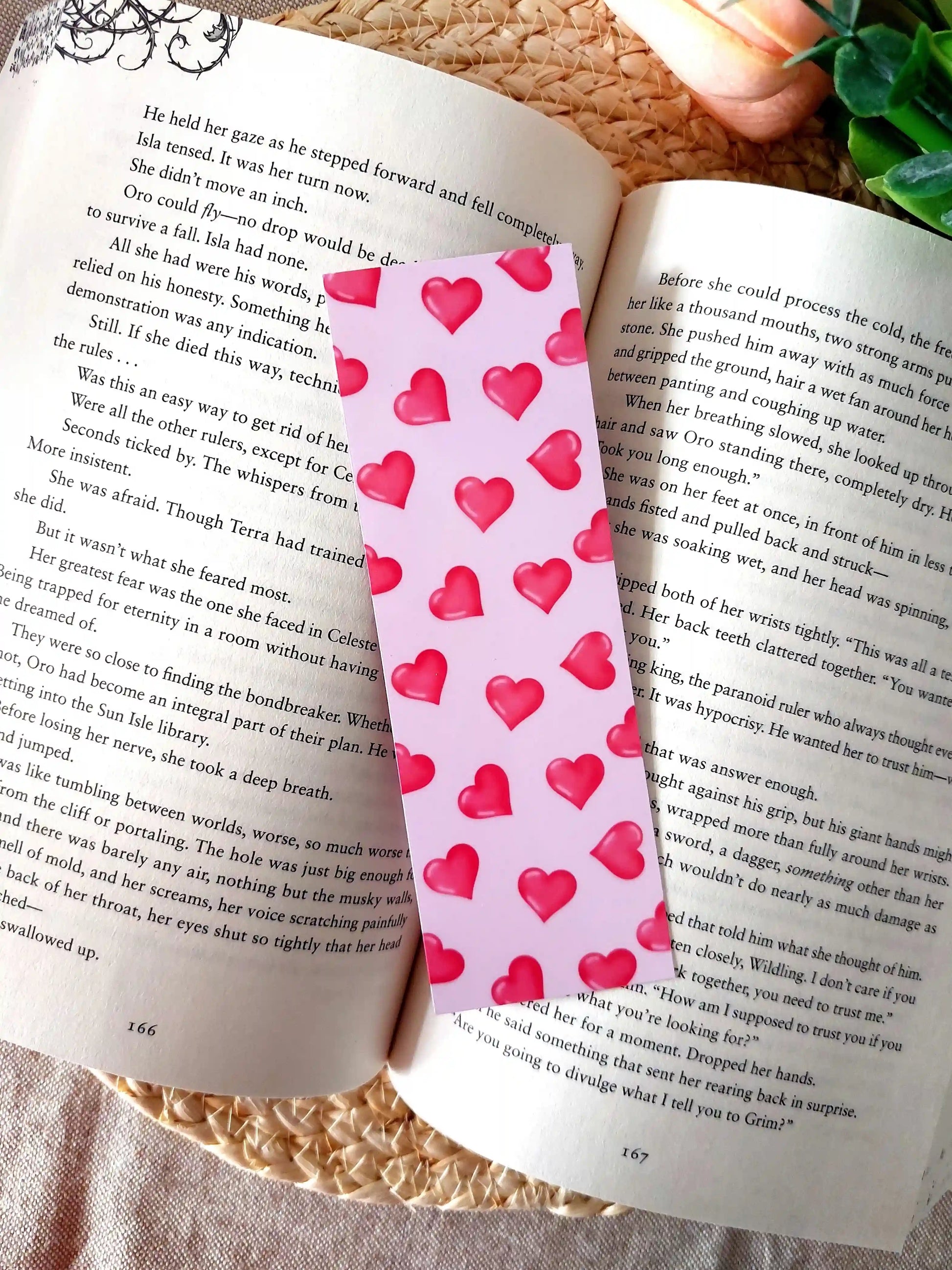 Bookmark featuring a pattern with  glossy red hearts on a pink background, resting on an open book.