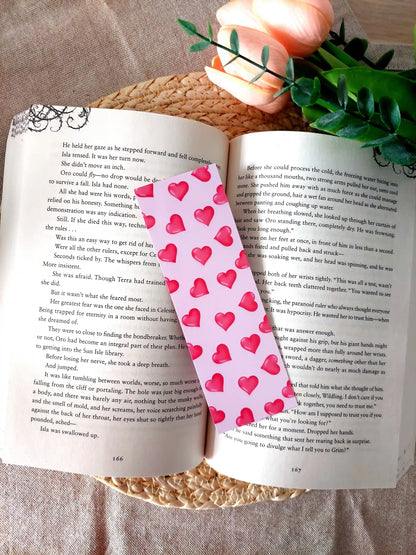 Bookmark featuring a pattern with  glossy red hearts on a pink background, resting on an open book.
