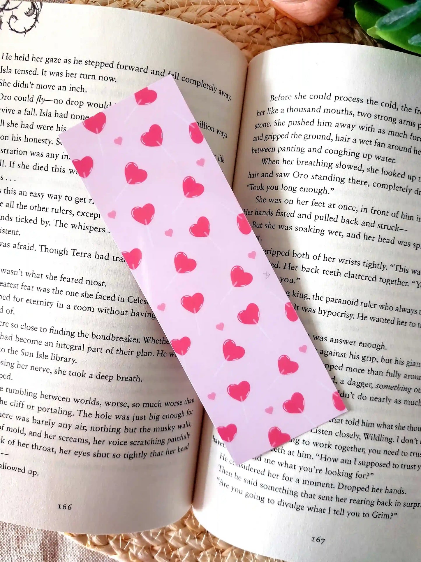 Bookmark featuring a pattern with  heart-shaped lollipops on a pink background, resting on an open book.