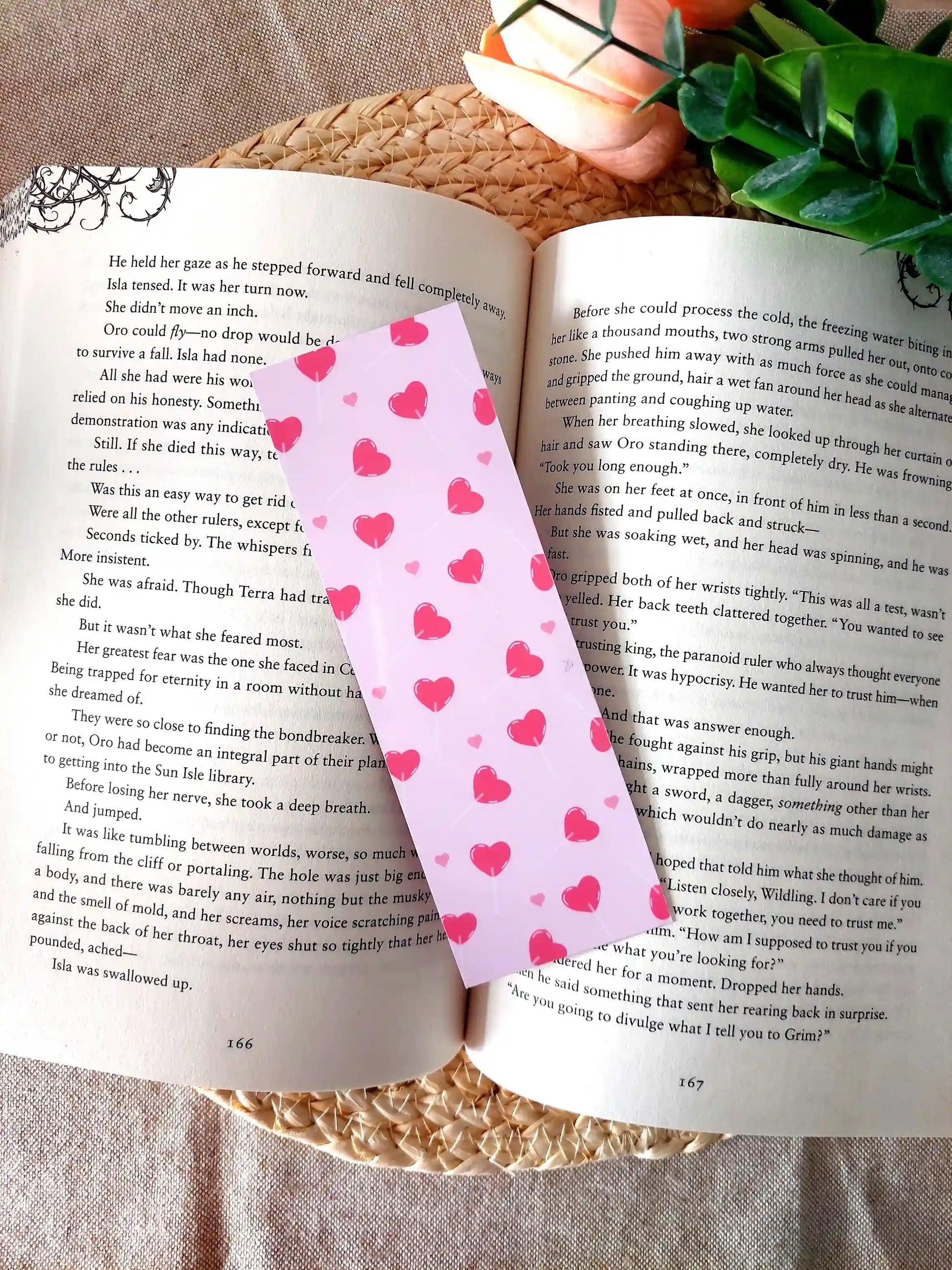 Bookmark featuring a pattern with  heart-shaped lollipops on a pink background, resting on an open book.