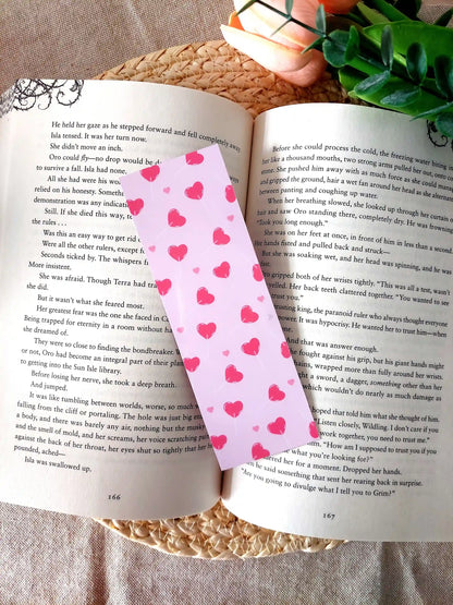 Bookmark featuring a pattern with  heart-shaped lollipops on a pink background, resting on an open book.