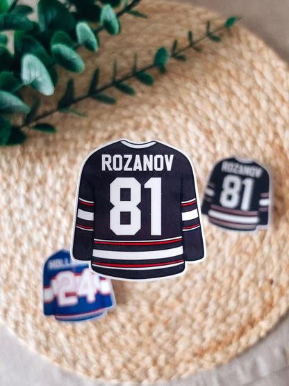 A die-cut sticker shaped like a blue hockey jersey reading "Rozanov 81" in white lettering with red and white stripes at the center of a woven rattan mat. 