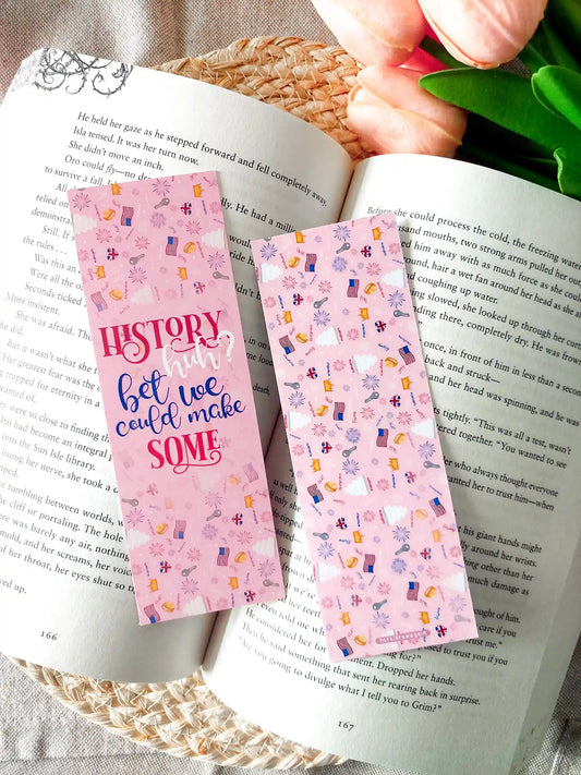 Two-sided Red, White & Royal Blue bookmark showing the front and back: the front features the quote "History, huh? Bet we could make some." in red and blue lettering on a pink background, while the back has a matching patterned design, resting on an open book.