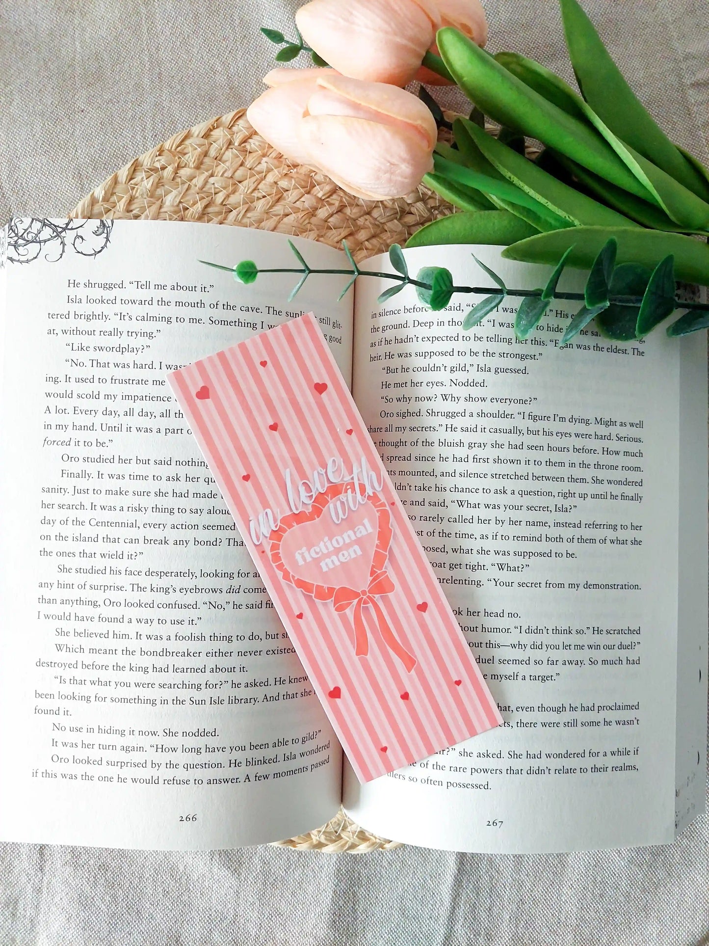 Bookmark with striped pink and peach background, small heart details and bow illustration, featuring the text "In love with fictional men", placed on an open book.