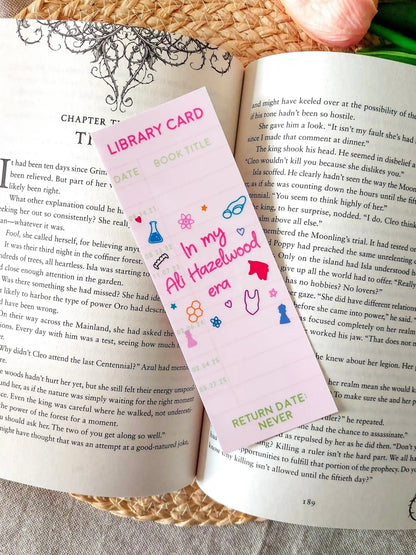 Bookmark designed like a library card, with the text “In my Ali Hazelwood era”, and small themed illustrations, resting on an open book.