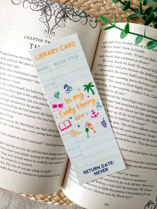 Bookmark designed like a library card, with the text “In my Emily Henry era”, and small themed illustrations, resting on an open book.