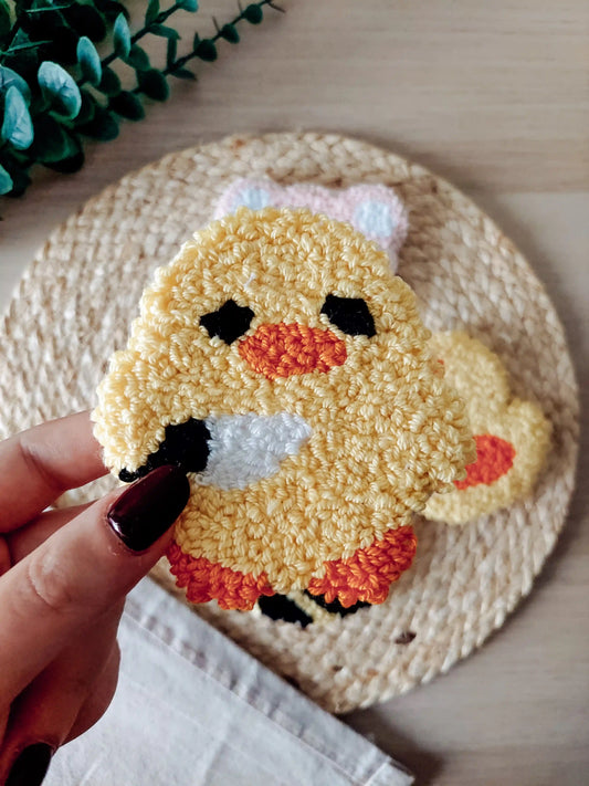 Handmade punch needle coaster, featuring a cute yellow duck with black eyes, orange beak and feet, holding a small knife.