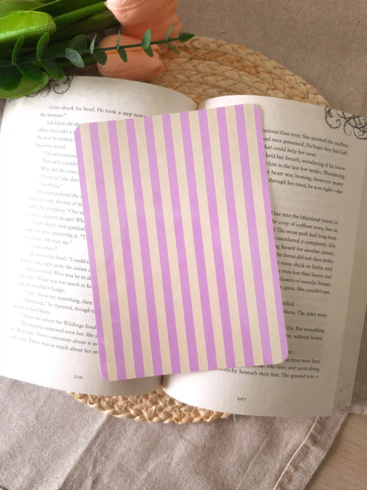 An e-reader insert with soft lavender and cream vertical stripes, placed on an open book resting on a woven rattan mat. 