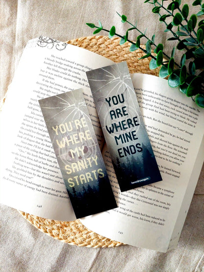 Leave Me Behind inspired bookmark displayed on an open book, featuring a forest and cracked glass design with the quote "You're where my sanity starts" and "You are where mine ends" split across front and back.