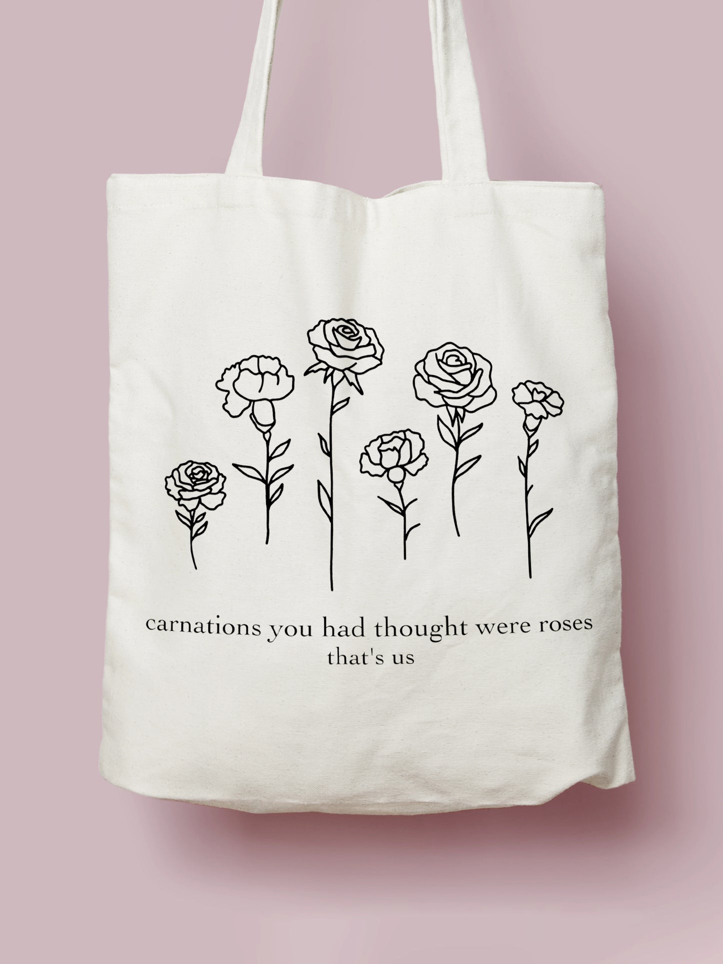Cotton canvas tote bag featuring black line art flowers and the lyric “Carnations you had thought were roses, that’s us,” photographed  on a soft pink background.