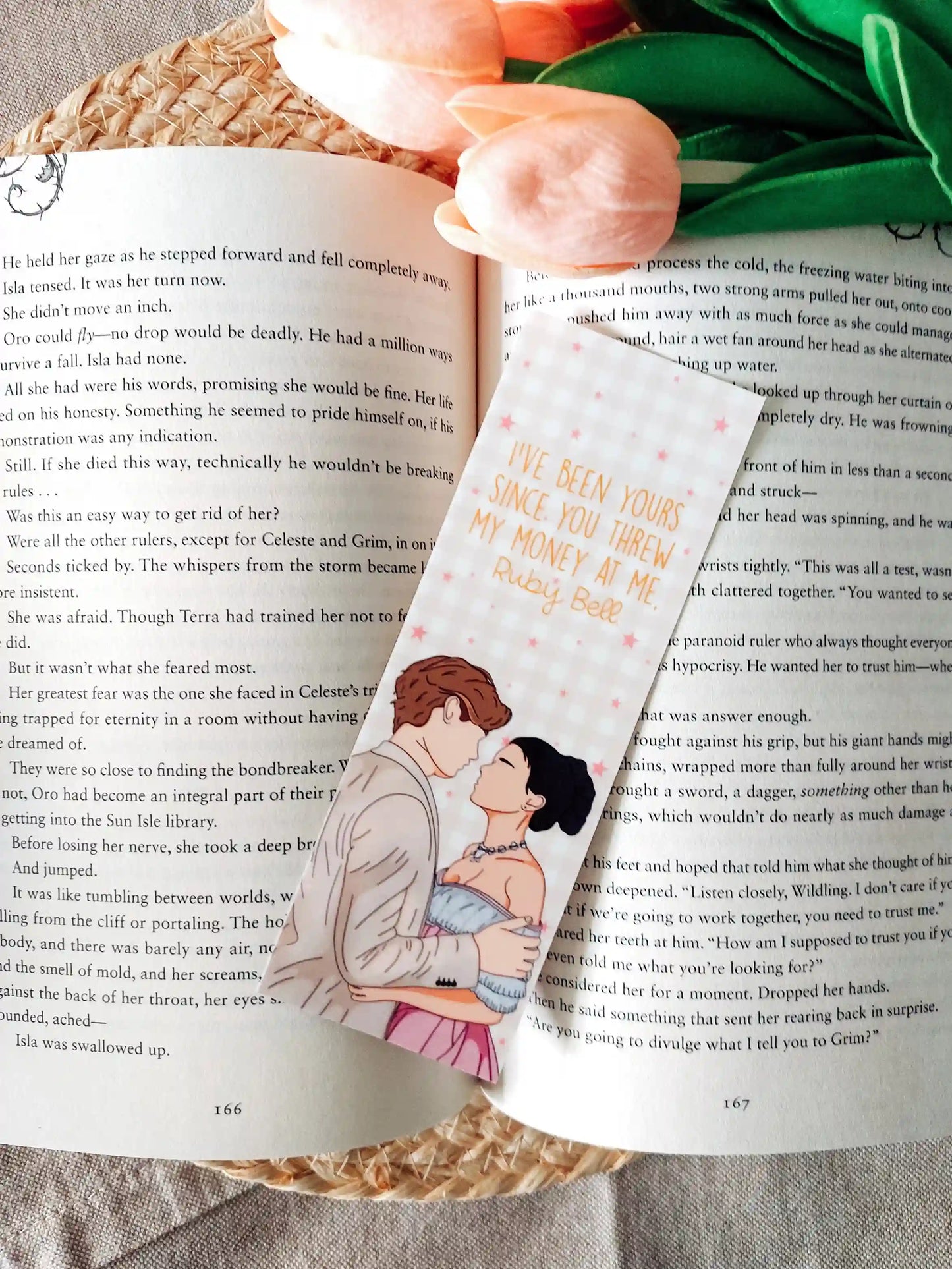Bookmark inspired by Maxton Hall featuring an illustration of Ruby and James, with the quote "I’ve been yours since you threw my money at me. Ruby Bell." printed on a gold gingham background, resting on an open book